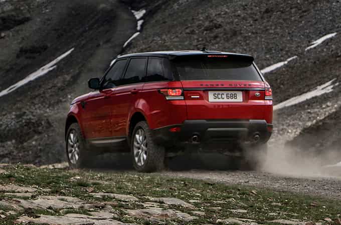 Range Rover Sport off-roading on rugged terrain rear side view.