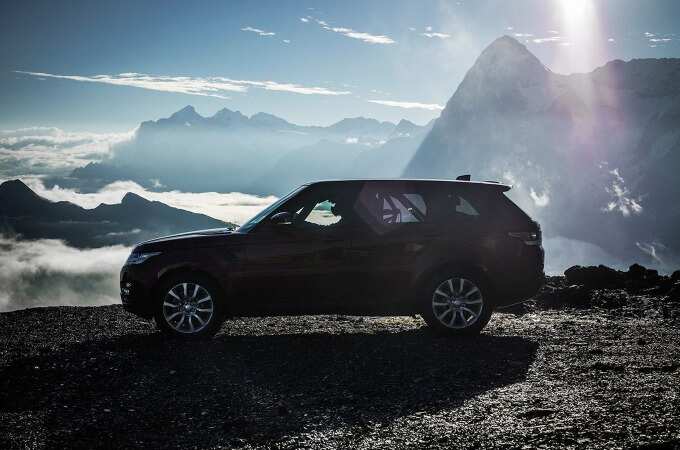 Range Rover Sport at the top of a mountain overlooking other mountain peaks above clouds. 
