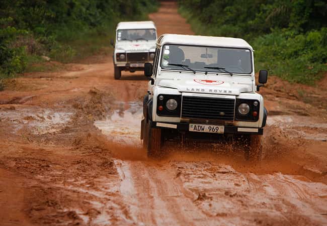Land Rover Defenders driving down a muddy trail.