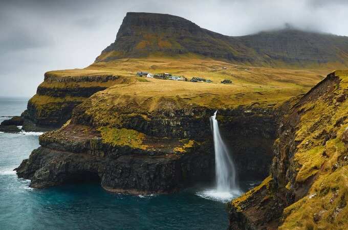 Faroe Islands sweeping landscape of steep cliffs, rugged terrain and waterfall.