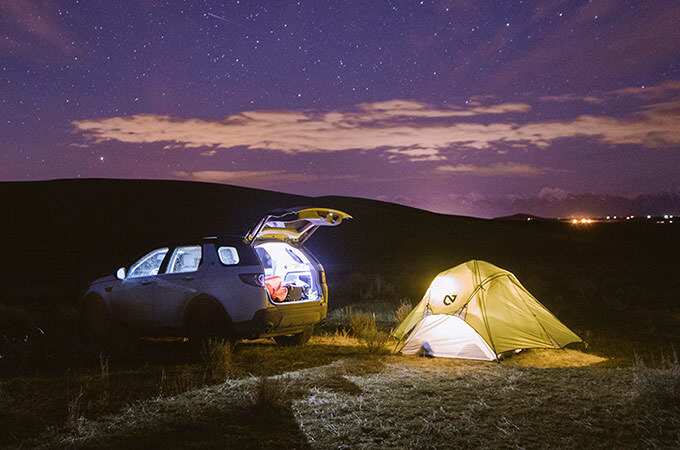 Land Rover Discovery Sport next to a pitched tent camping under the night sky.