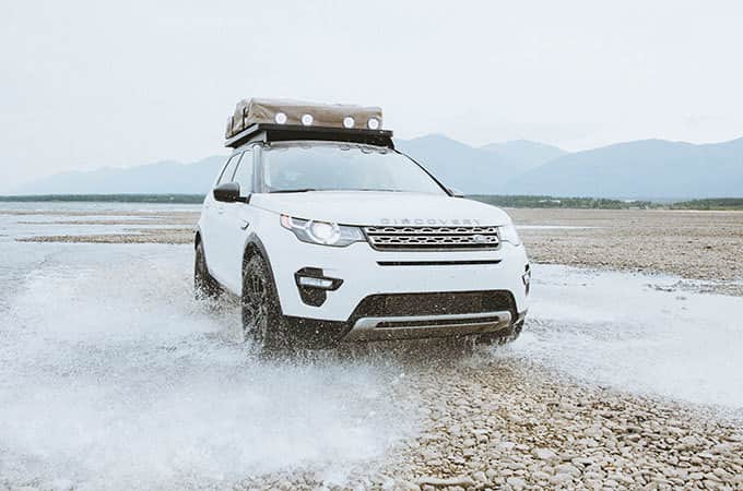 Land Rover Discovery Sport wading through shallow water on rocky terrain in Alaska front side view.