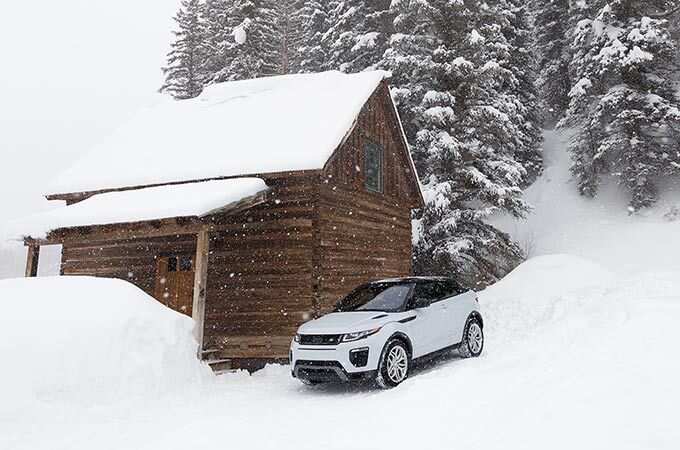 Range Rover Evoque Convertible on a snowy hill next to a cabin.