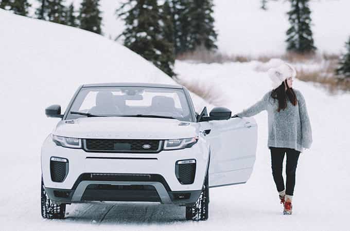 Lady with a fur hat steps out of a Range Rover Evoque Convertible against a winter landscape. 