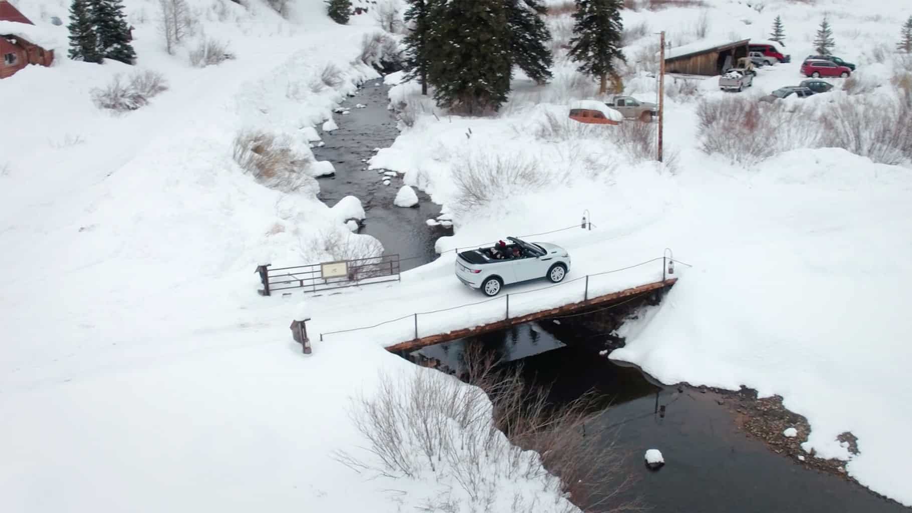 Range Rover Evoque Convertible top down crossing a snow covered bridge over a stream.