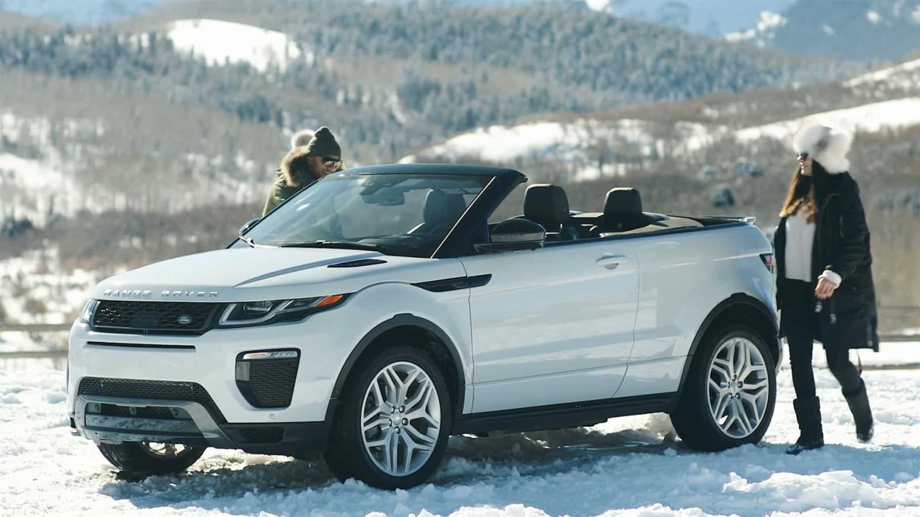 Range Rover Evoque Convertible top down on snow with driver and passenger getting into vehicle.