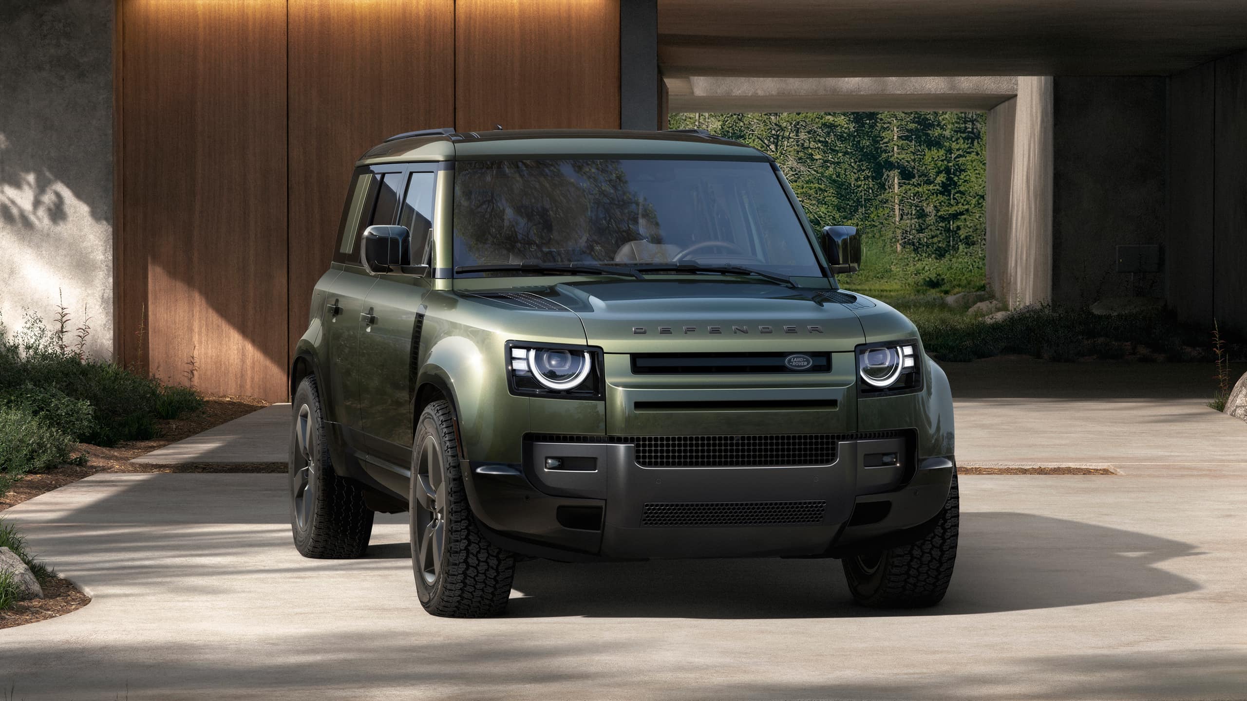 Front view of a green Defender parked outside a modern house.